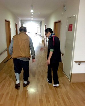 廊下を歩く入居者と職員。木質床で明るく清潔な共用部。